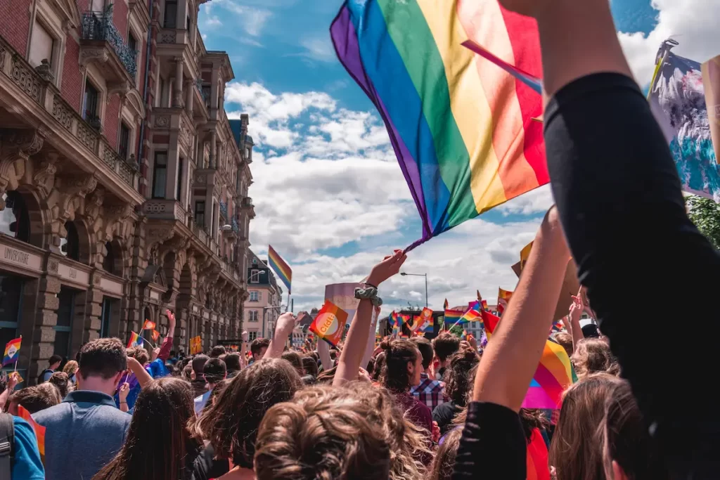 プライドパレードの写真。町の大通りにたくさんの人がつめよせ、LGBTQのシンボルである虹の旗を振っています。