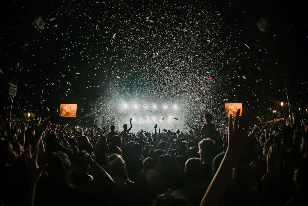 音楽フェスティバルのイメージ写真。暗闇のむこうに明るい巨大なステージがあり、その前には数えきれない人が手を仰いで音楽を楽しんでいます。